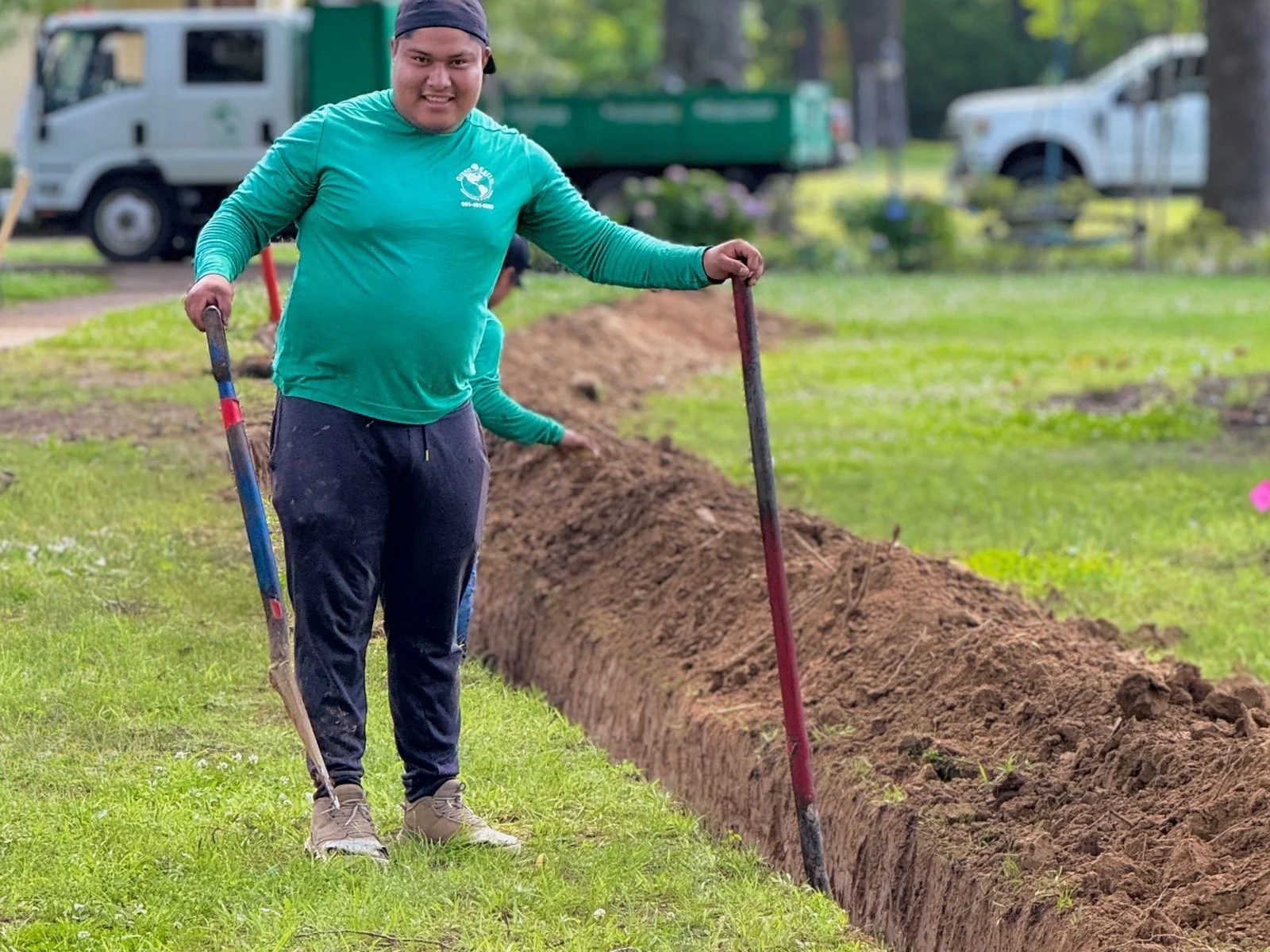 Green Earth crew member digging a sloped drainage trench with a shovel in a wet Germantown, TN lawn