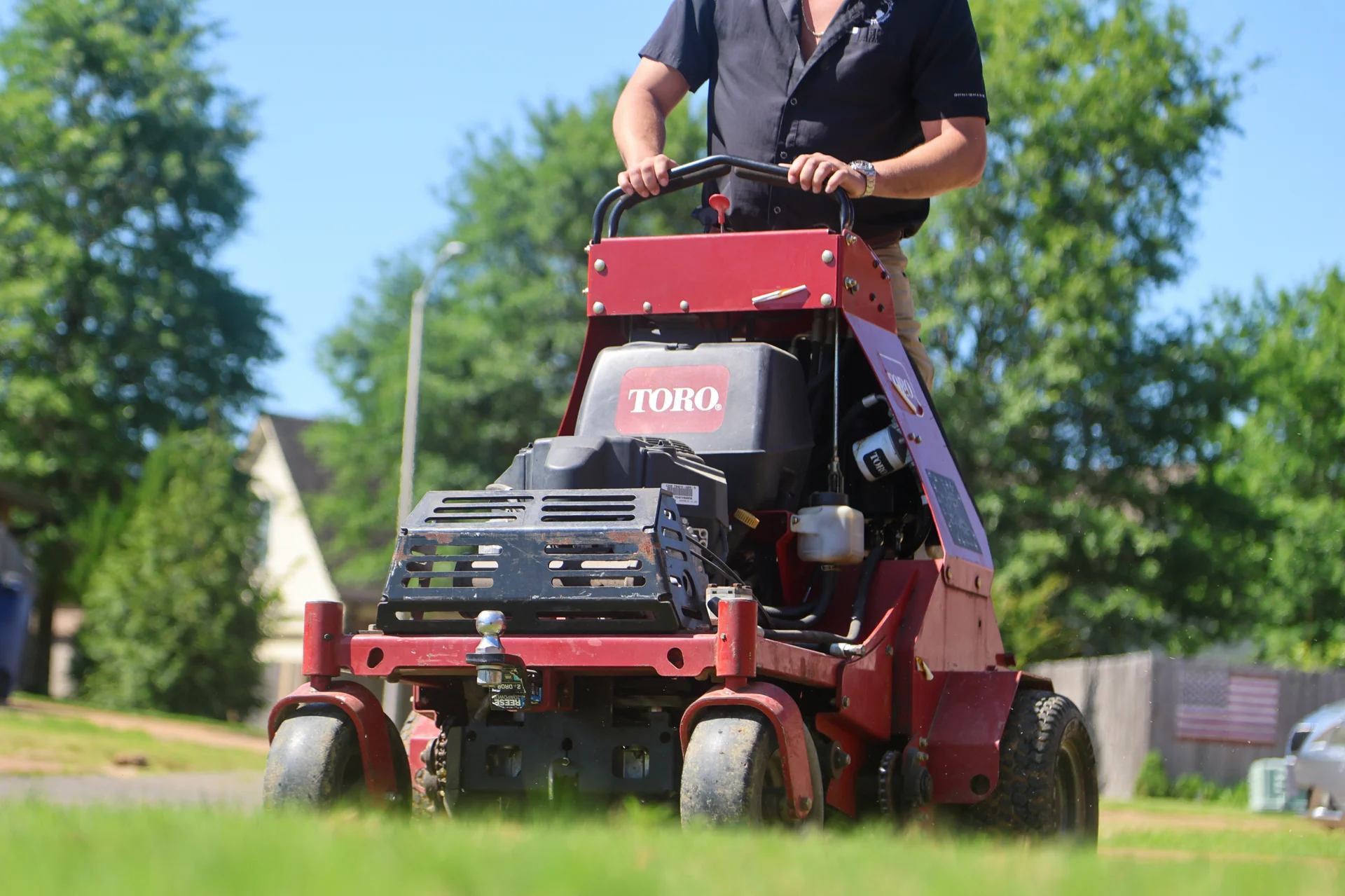 A red Toro stand-on lawn aerator pulling core plugs on a residential green lawn during a spring aeration service in Germantown, Tennessee.