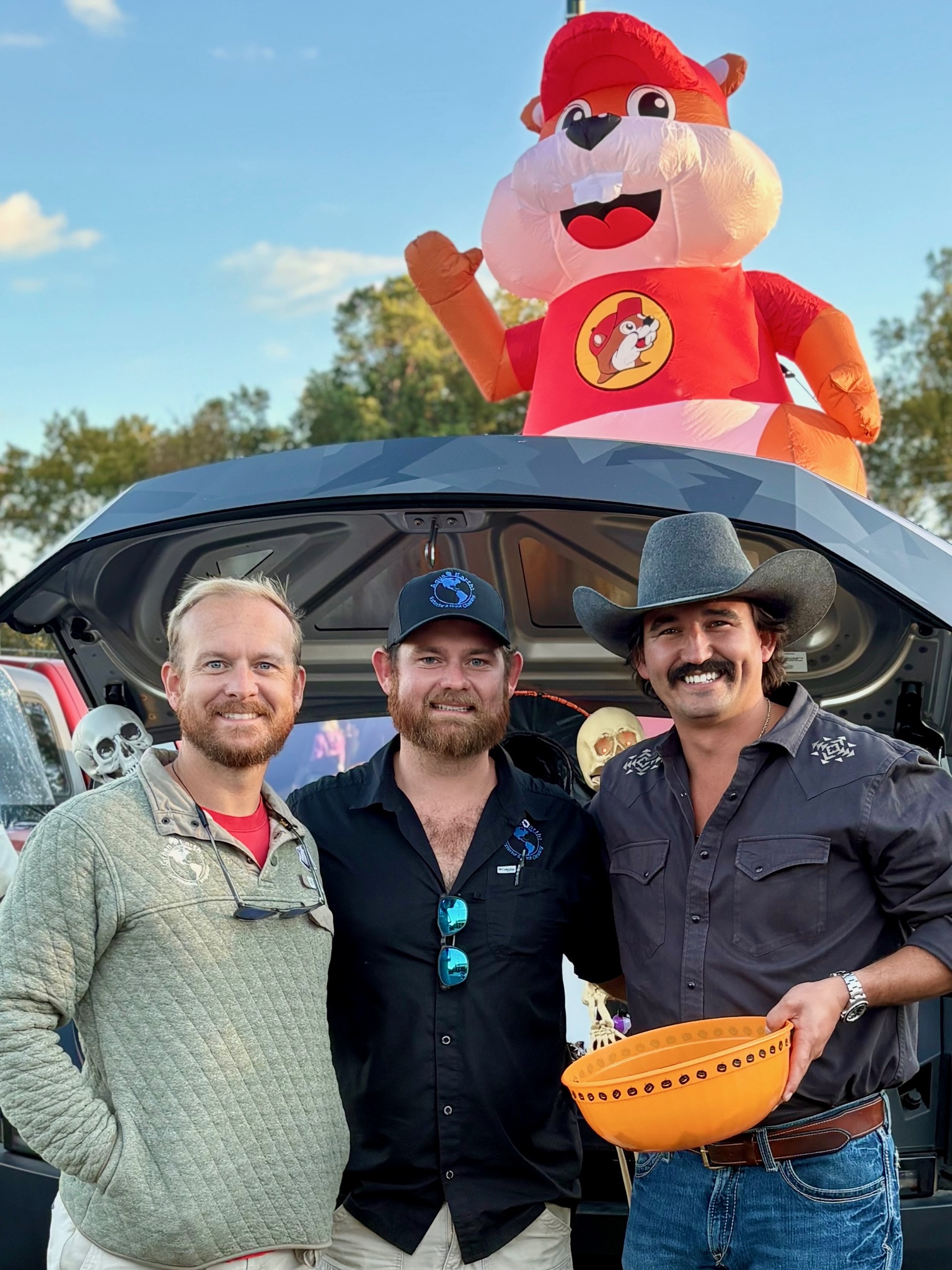 Three Green Earth crew members at a trunk-or-treat setup with a Buc-ee beaver inflatable and candy bowl