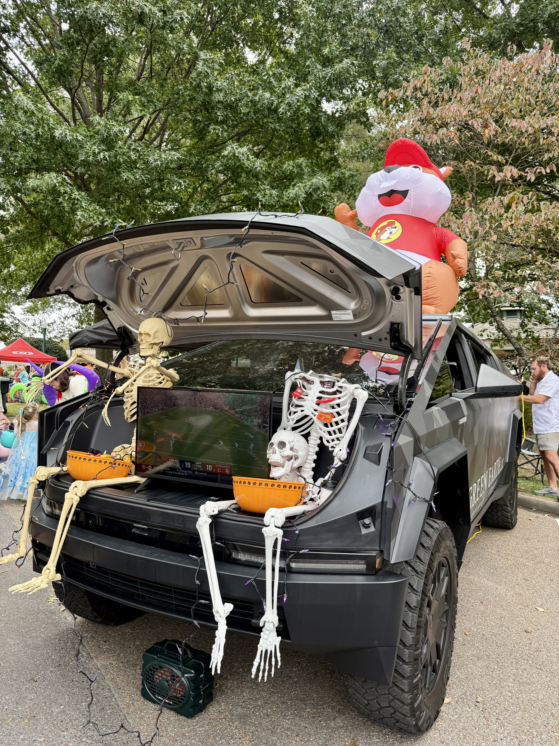 Green Earth Cybertruck frunk decorated for trunk-or-treat with skeletons, candy, and a Buc-ee beaver inflatable