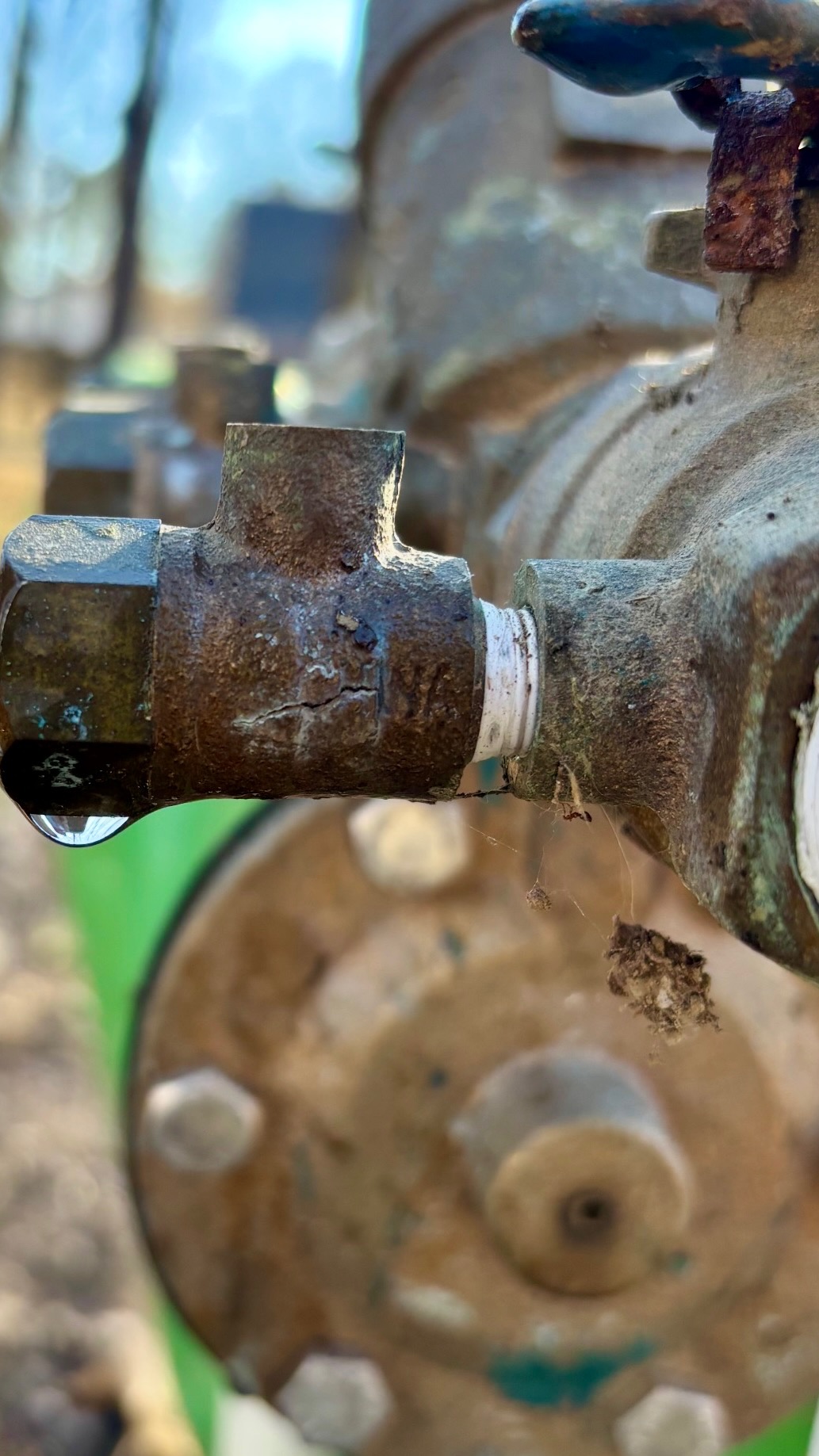 Close-up of a cracked brass irrigation fitting dripping water after freeze damage