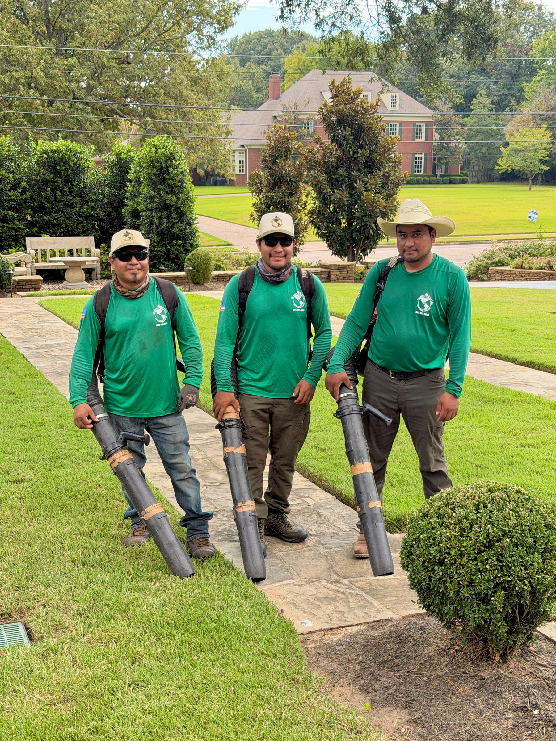 Three Green Earth crew members holding commercial leaf blowers on a lawn
